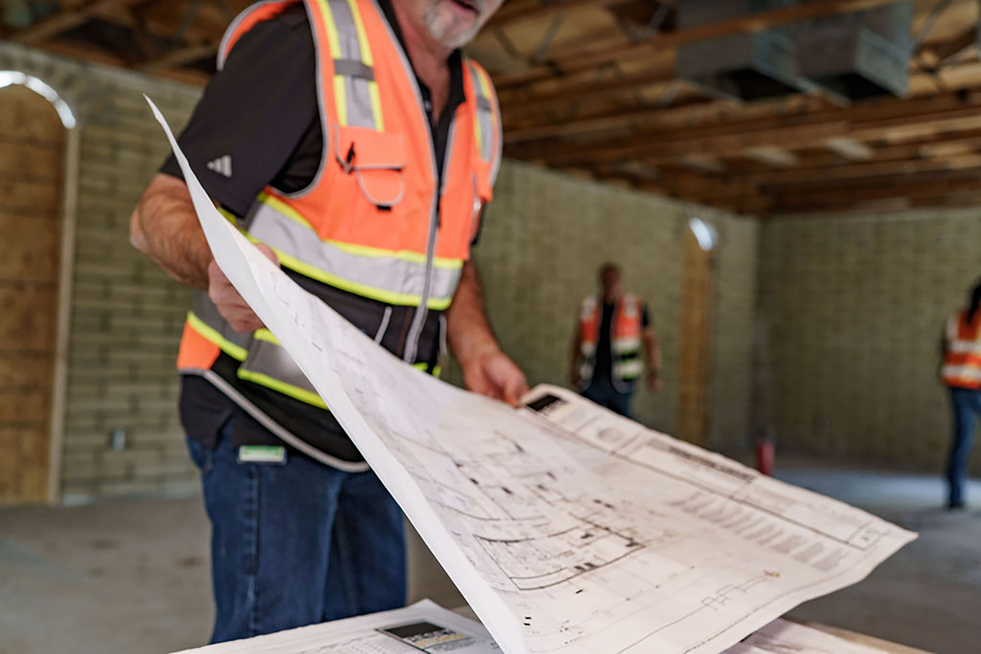 A construction worker in a safety vest examines architectural blueprints inside a partially built structure, highlighting the progress of commercial construction in Arizona.